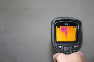 Inspector using an infrared camera to detect unseen moisture in a wall