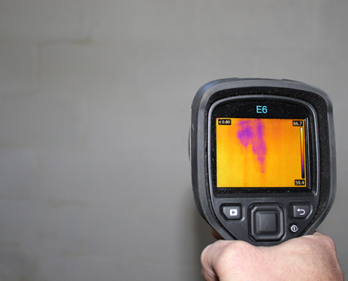 Inspector using an infrared camera to detect unseen moisture in a wall